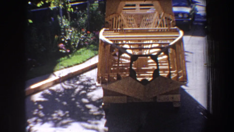 1965 Yucaipa home-movie frame showing the wooden slat object from a low angle, surrounded by pavement, greenery, and bright shadow patterns.