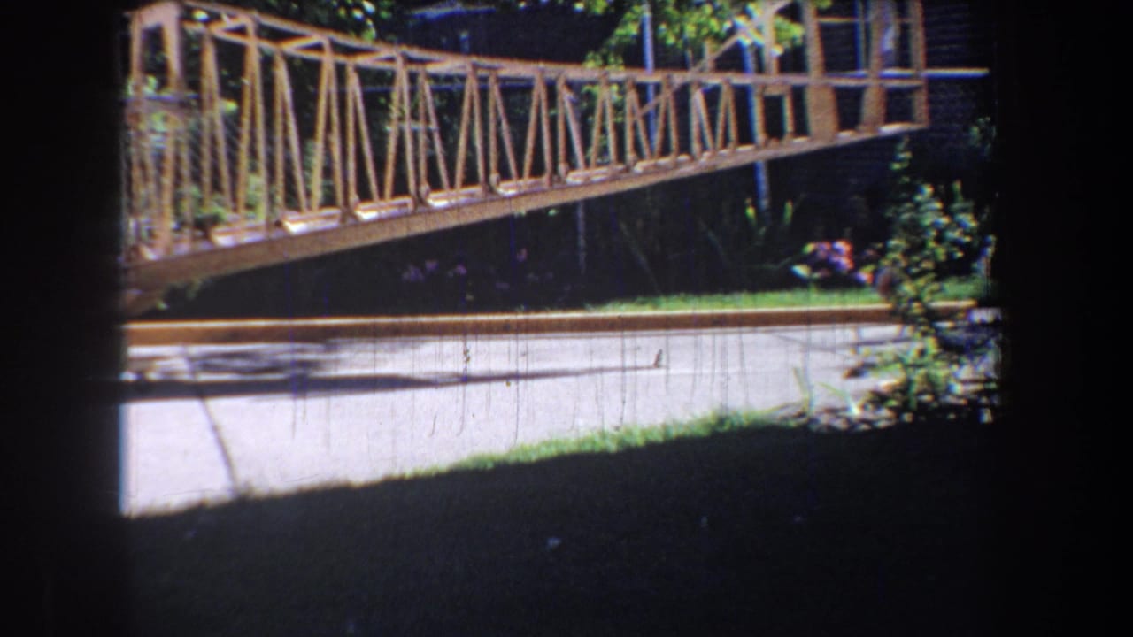 Bridge railing and truss span above a road with trees and a small distant figure.