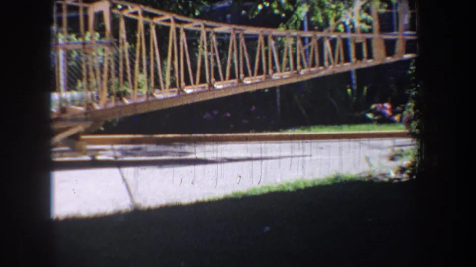 1965 Volmer, Yucaipa frame showing the bridge truss, fenced side rail, bright pavement, foliage, and dark foreground film-shadow areas.