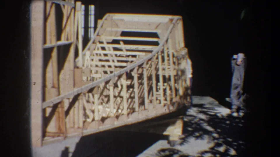 1965 Volmer Yucaipa frame showing a timber bridge or pavilion structure beside a wall, with an adult man nearby.