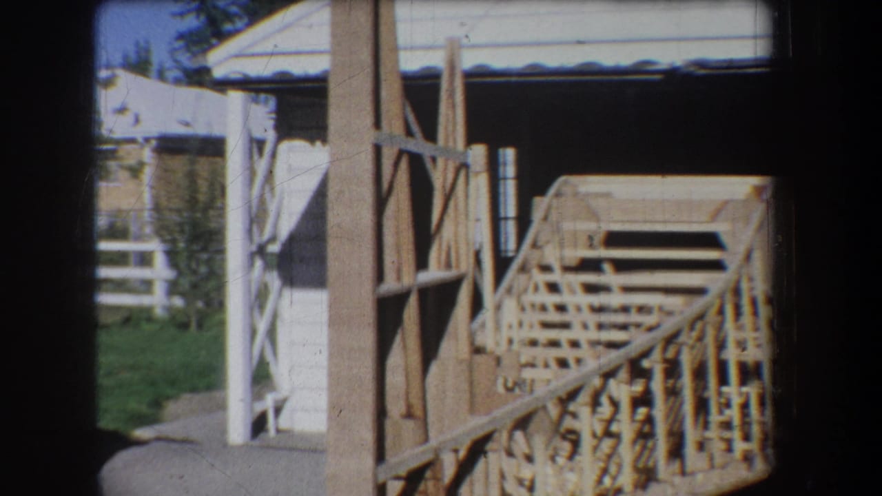 Wooden model structure beside garage posts with white fence and lawn visible outside.