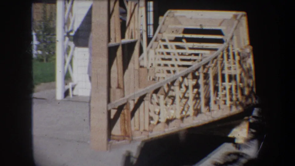 1965 Yucaipa frame showing the handmade wooden model at the garage threshold, partly obscured by dark framing and workshop shadows.