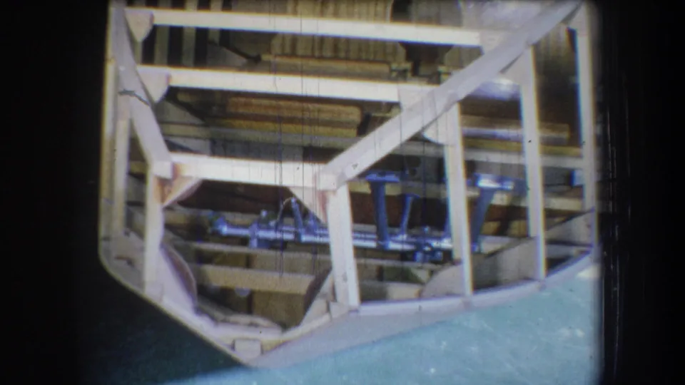 The camera looks beneath the unfinished wooden structure, showing beams, supports, and shadowed underside framing.