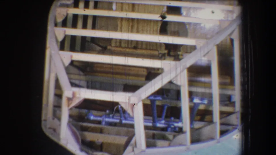 1965 Yucaipa-area home-movie frame showing an unfinished wooden boat structure with ribs, cross beams, and metal hardware.