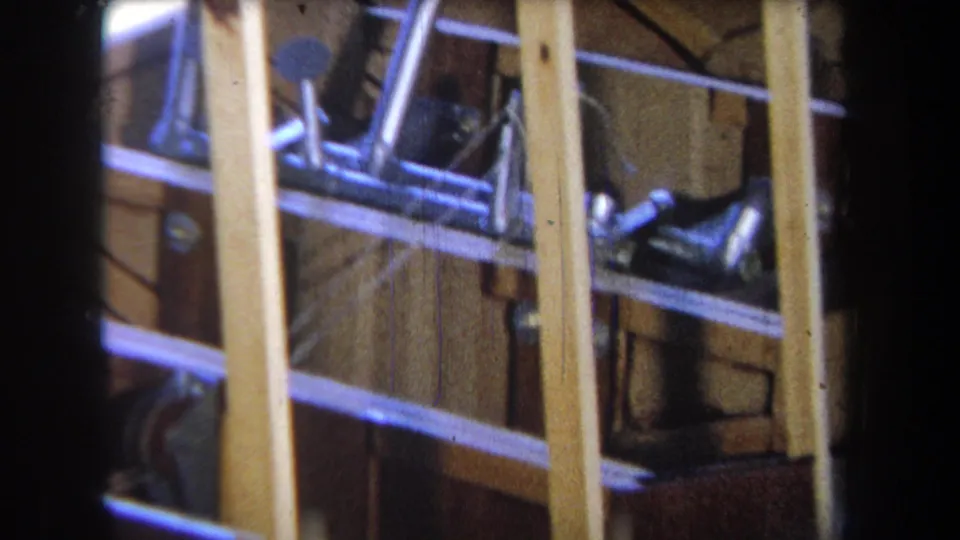 Closer 1965 home-movie detail of the boat under construction, with vertical timber supports, hull planking, and dark metal fittings.
