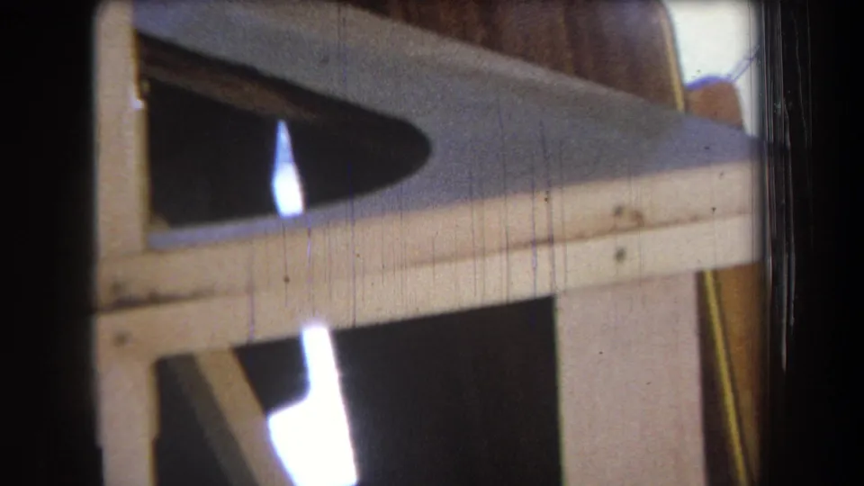 Close 1965 Yucaipa-area 8mm view of a horizontal beam, vertical studs, and a shadowed opening in an unfinished structure.