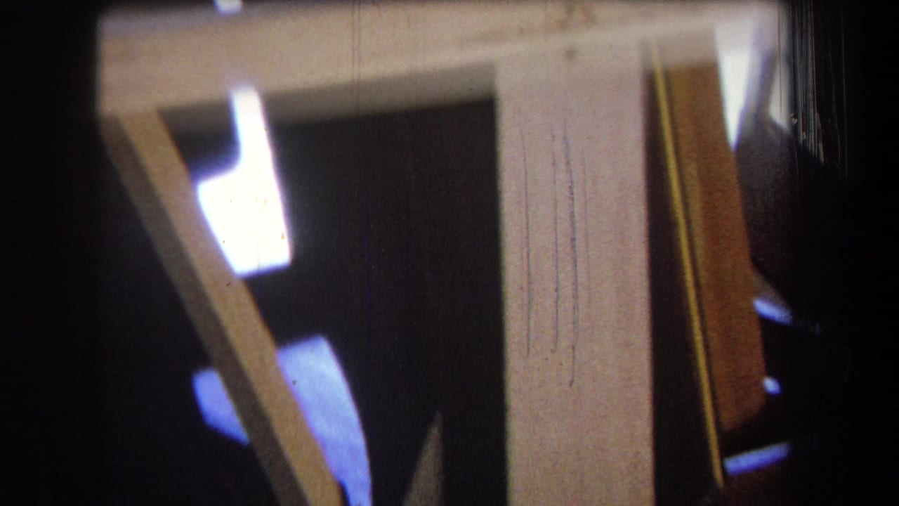 1965 Yucaipa 8mm frame showing yellow wood supports, angled boards, and dark interior space with a small bright light area.