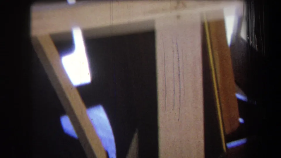 1965 Yucaipa 8mm frame showing yellow wood supports, angled boards, and dark interior space with a small bright light area.