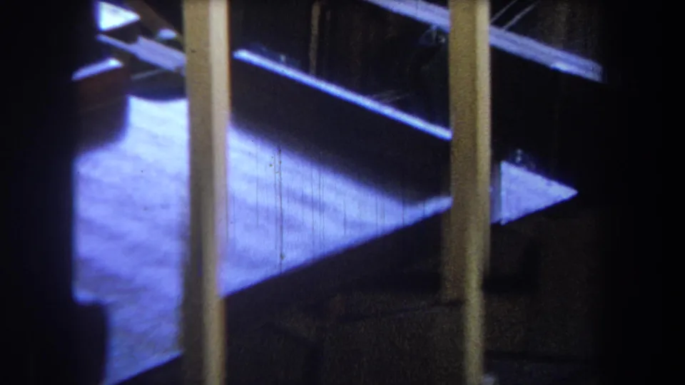 1965 Yucaipa home-movie frame with yellow uprights, blue-lit flooring, and a shadowed gap beyond the structure.