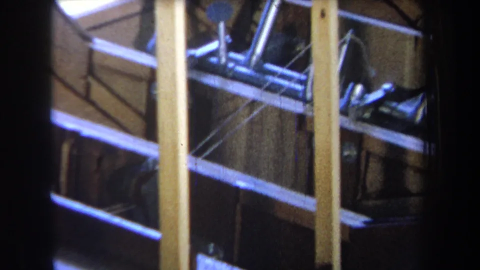 1965 Yucaipa 8mm frame showing silver metal tubing and rods behind yellow vertical framing inside a shadowed work area.