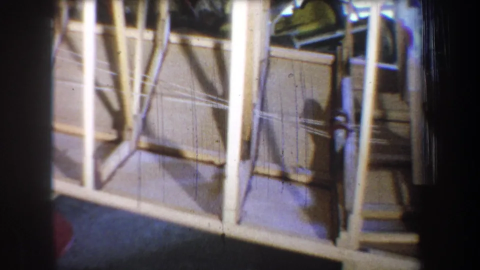 1965 home-movie frame showing a side section of the unfinished wooden boat, including crossed bracing and floor-level detail.