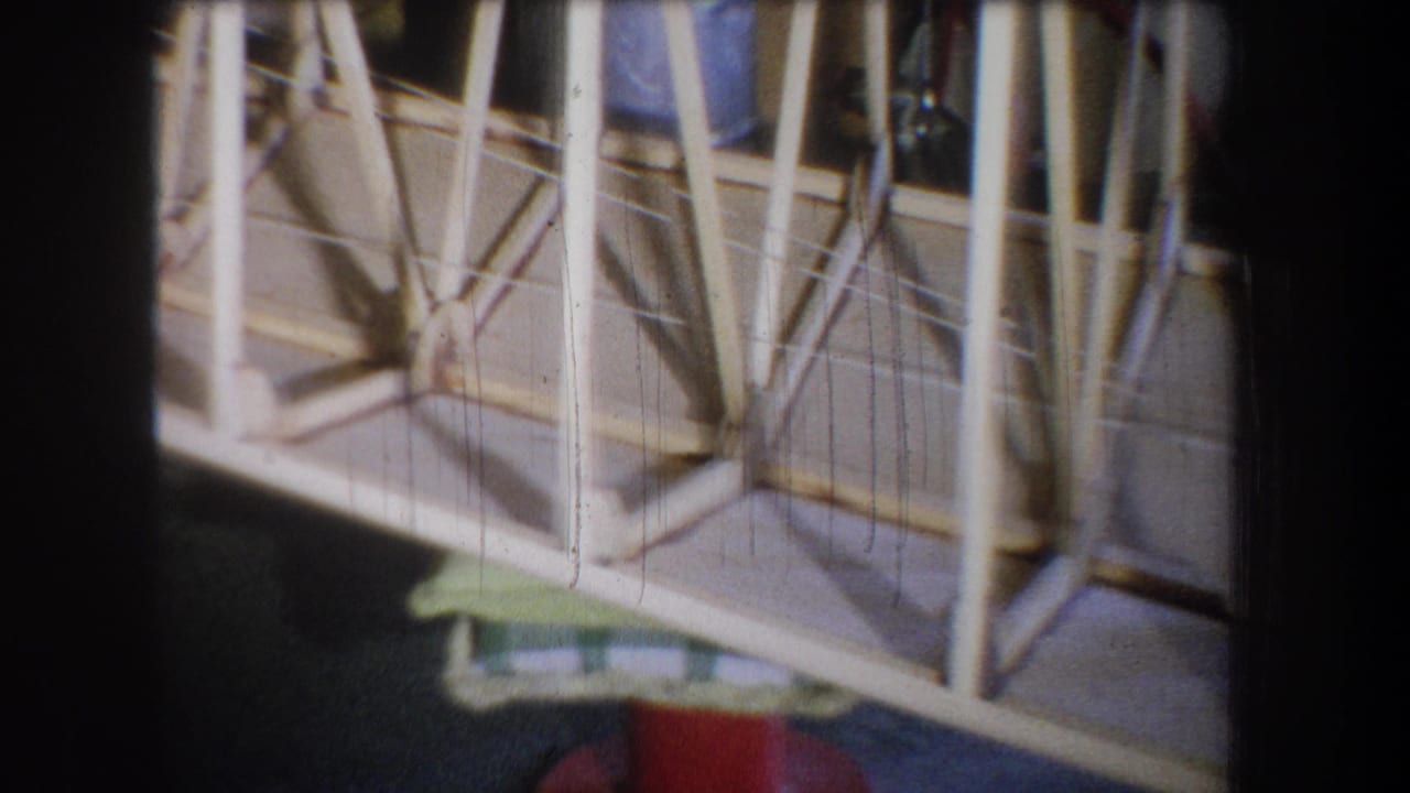 1965 Volmer Yucaipa home-movie frame showing a close view of a pale wooden truss structure with diagonal bracing and dark floor below.