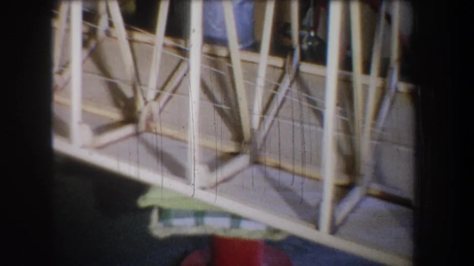 1965 Volmer Yucaipa home-movie frame showing a close view of a pale wooden truss structure with diagonal bracing and dark floor below.