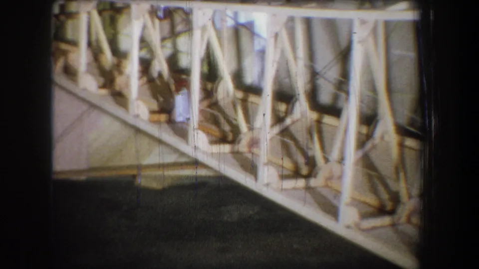 Close 8mm view of the wooden truss structure near the end of the clip, with dense bracing, pale wood, and dark floor visible.