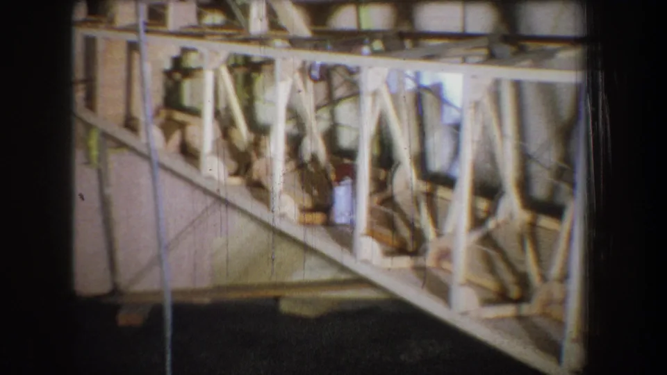 1965 Yucaipa-area 8mm frame showing exposed wood framing, metal braces, cords, and yellow support racks inside construction.