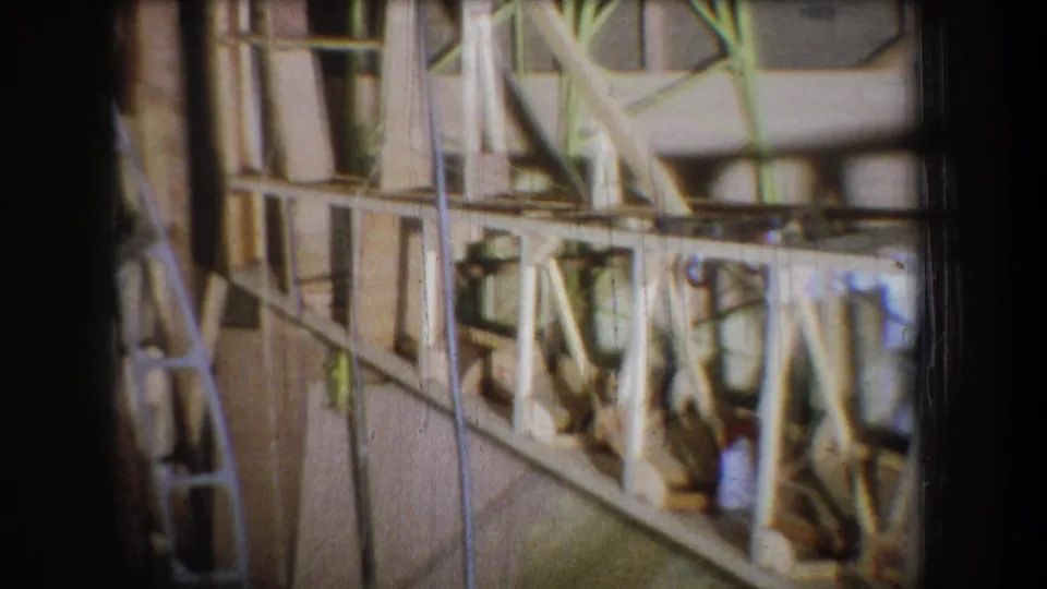 1965 Yucaipa-area 8mm view of an unfinished building interior with wood members, braces, cords, and yellow-painted supports.