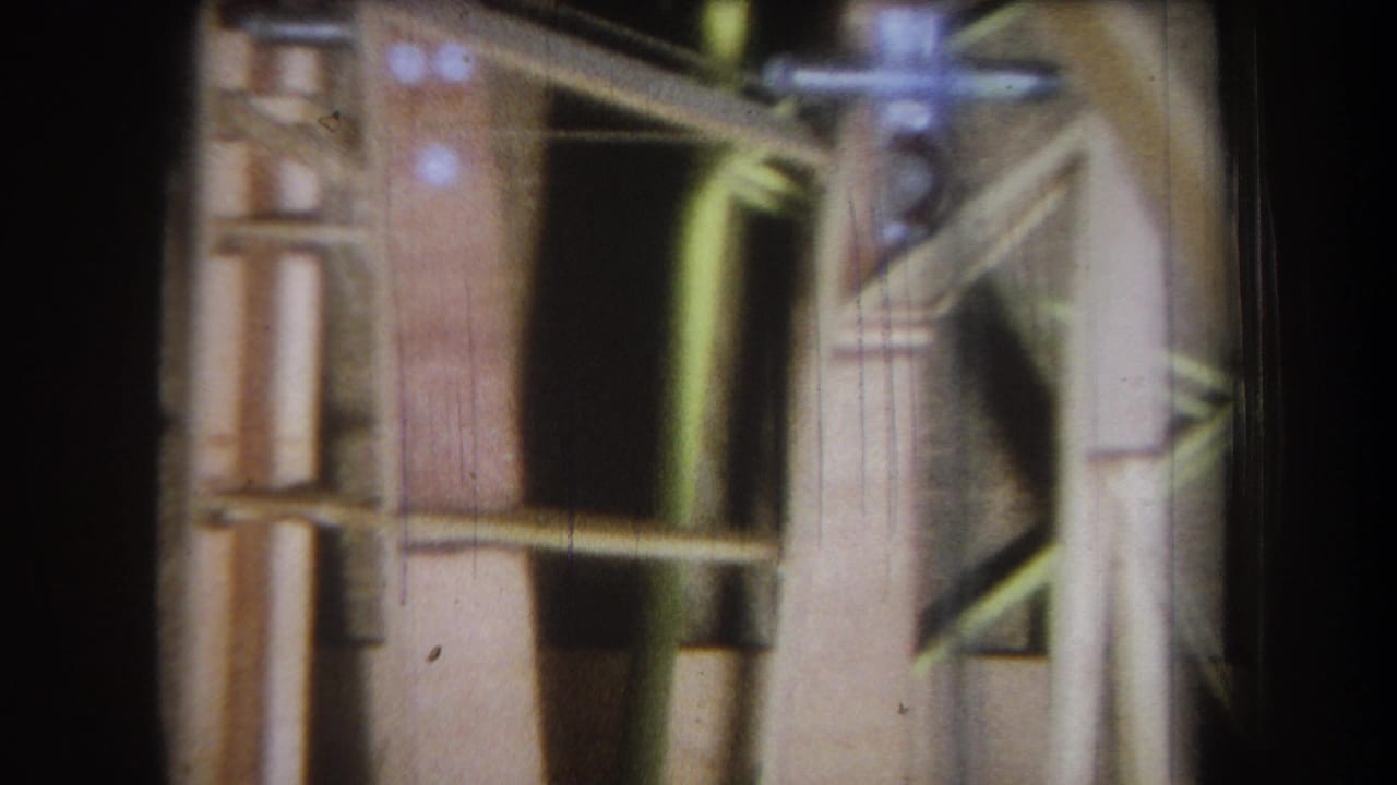 1965 Yucaipa home-movie frame showing close wooden construction framing, metal fittings and a shadowed mechanical opening.
