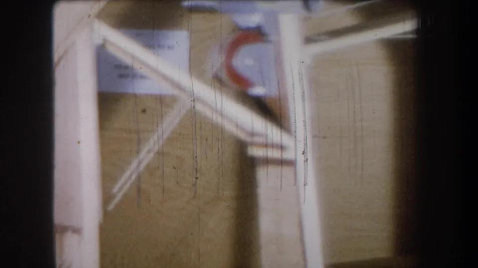 Soft 8mm frame from the supplied 1965 Yucaipa clip showing pale timber supports, metal pieces and a red curved marking.
