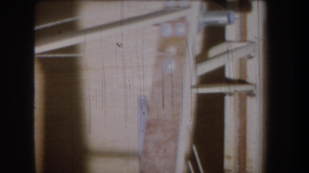 1965 Yucaipa 8mm frame showing a dim wooden garage or storage interior with shelf-like boards, vertical supports, scratches, and dust.