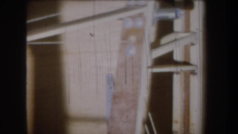 1965 Yucaipa 8mm frame showing a dim wooden garage or storage interior with shelf-like boards, vertical supports, scratches, and dust.