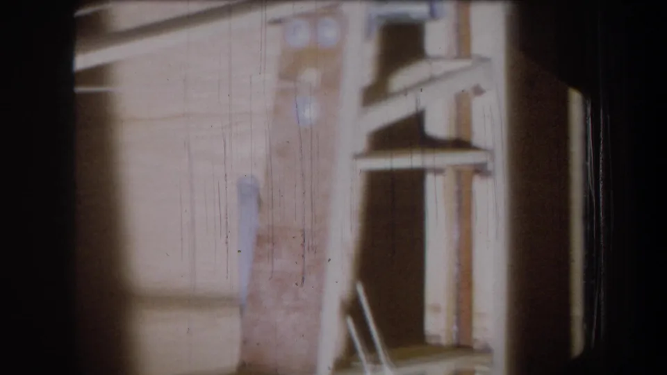 1965 Yucaipa home-movie frame of a static wooden garage view, with a shelf or ladder-like structure and pronounced 8mm wear.