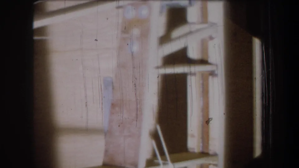 1965 Yucaipa 8mm still showing a dim domestic garage or storage corner with wood boards, a dark recess, and aged film marks.
