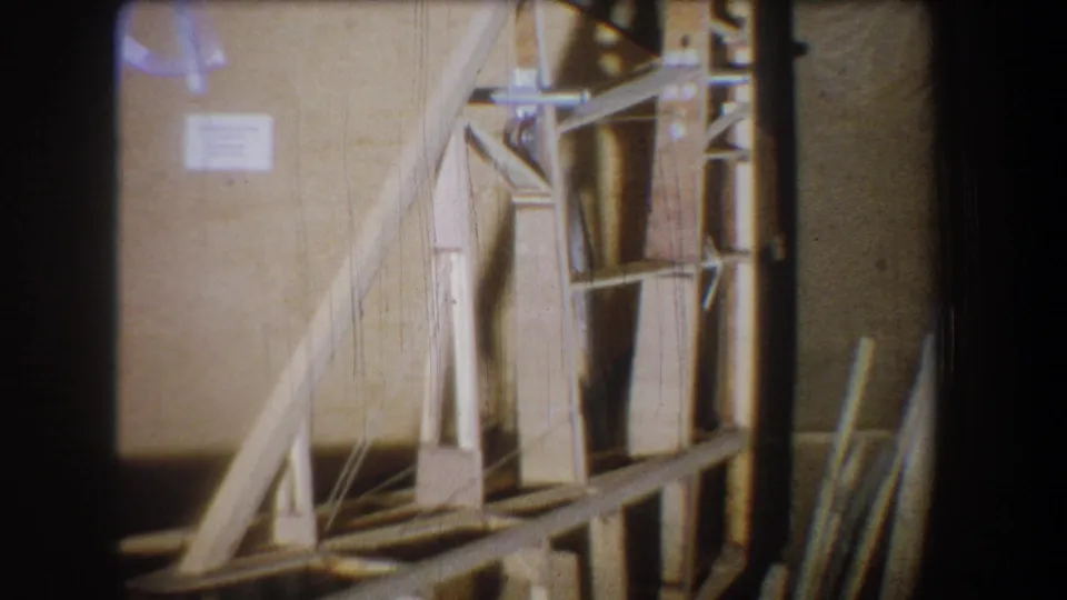 1965 Yucaipa home-movie frame showing the wooden construction model from a slightly shifted angle, with bracing and upright elements visible.