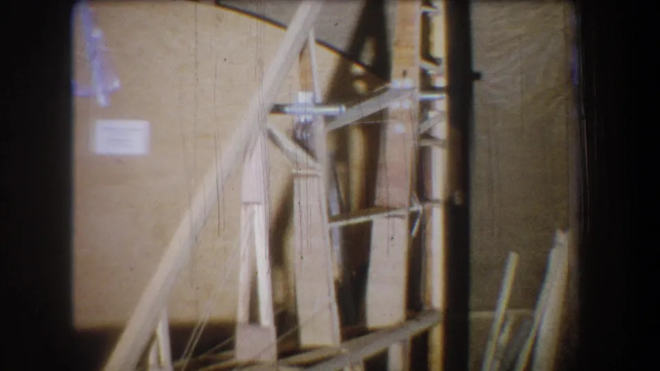 1965 Yucaipa 8mm frame with the wooden model filling much of the view, showing angled beams, vertical supports, and a dim background wall.