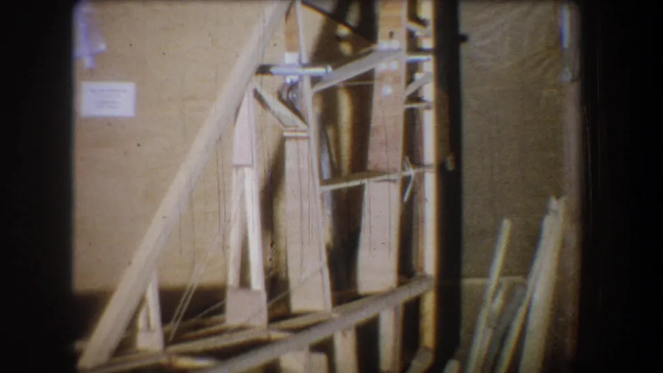 Final 1965 Yucaipa frame showing the wooden construction model with braces, upright posts, wall label, and visible 8mm film borders.