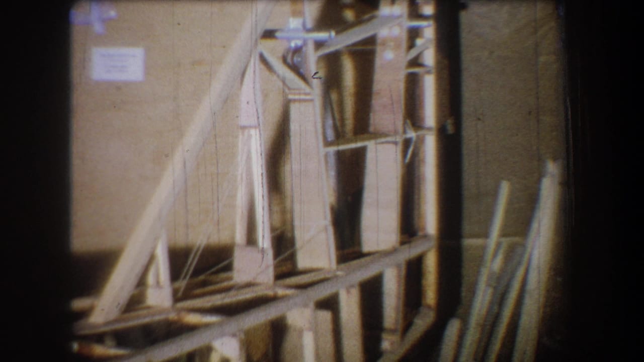 1965 Yucaipa 8mm frame showing a wooden structure, shelves, and stacked materials in a dim interior storage area.