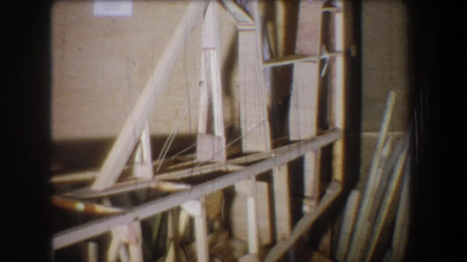 1965 Yucaipa home-movie frame with wooden supports, shelving, and stacked planks inside a storage or workroom space.
