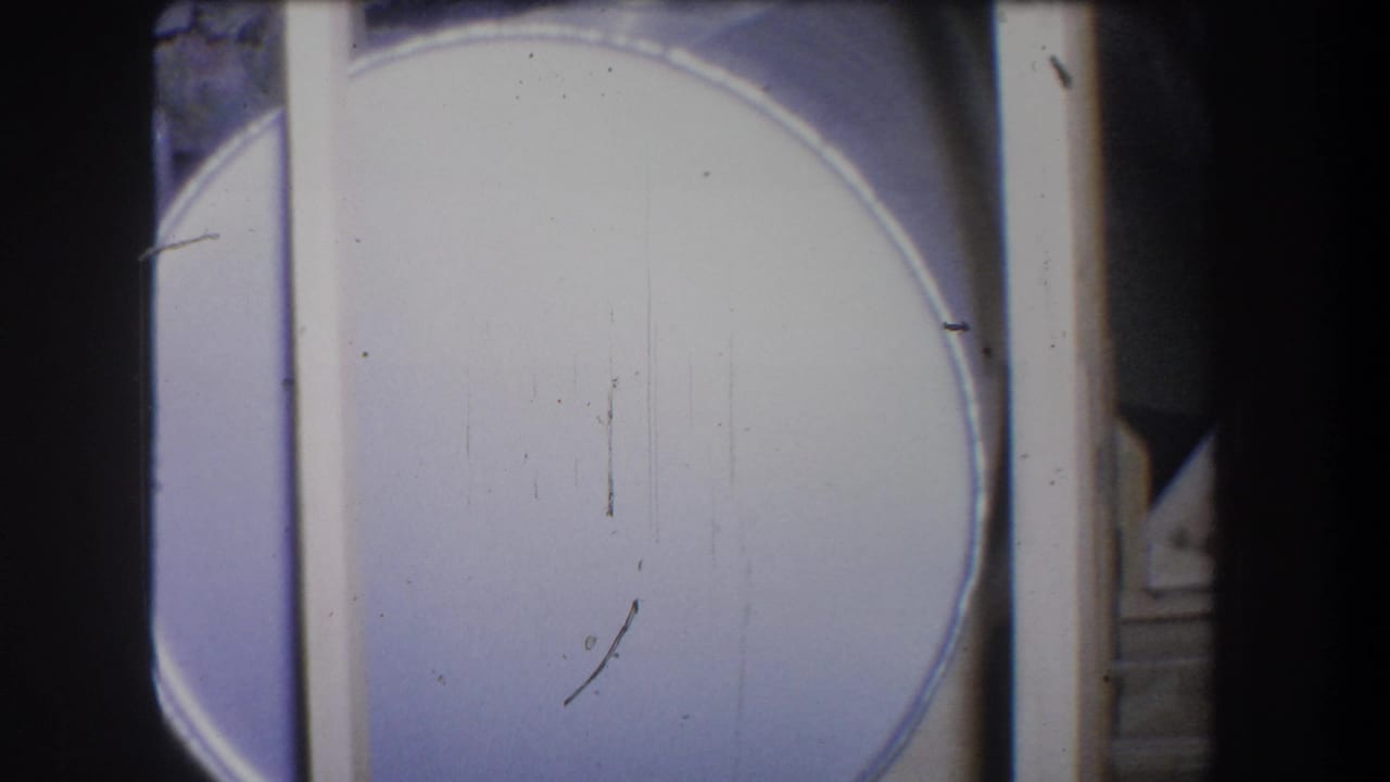 Large pale cylindrical metal container beside dark vertical framing.