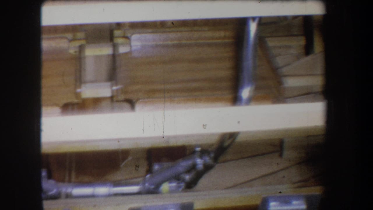 1965 Yucaipa-area 8mm frame showing the inside of an unfinished wooden boat hull with pale ribs, planks, and small metal hardware.