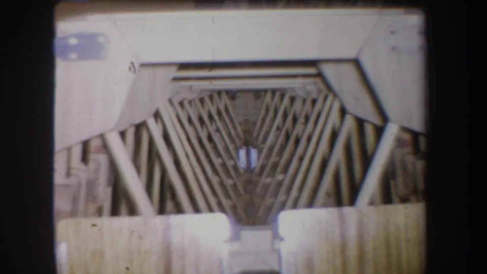 A closer 1965 8mm view of angled wooden framing in a warehouse-like interior in Volmer Yucaipa, California.
