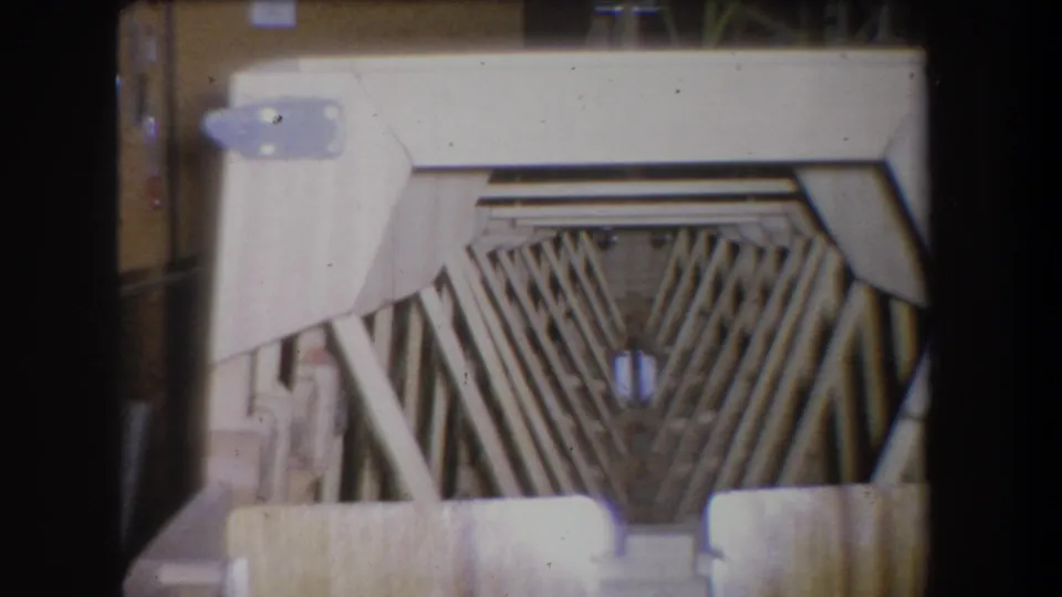 Final 1965 8mm frame of the wooden scaffold pattern in a warehouse-like interior, with faded color and visible film wear.