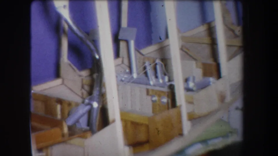 1965 Yucaipa 8mm frame with a soft handheld view of the homemade model’s wooden frame, white supports, and metal fittings.