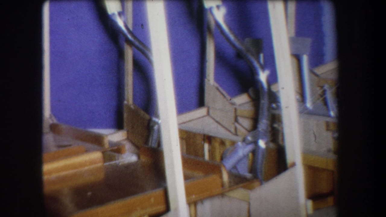 1965 Yucaipa home-movie frame showing varnished wooden stairs, white metal railings, and a deep blue wall in close view.