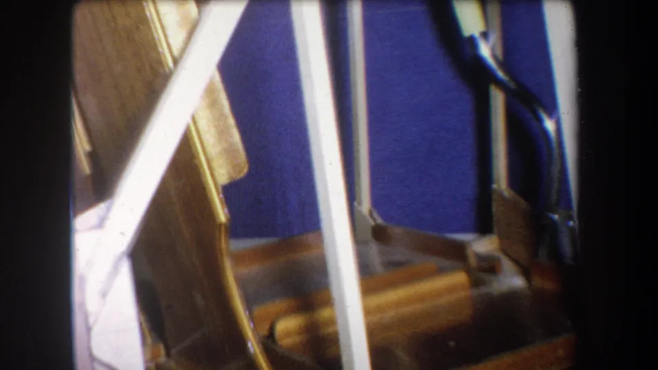 1965 Yucaipa home-movie frame showing the lower staircase area, blue wall, white railing, wood trim, and a crumpled light object near the stairs.