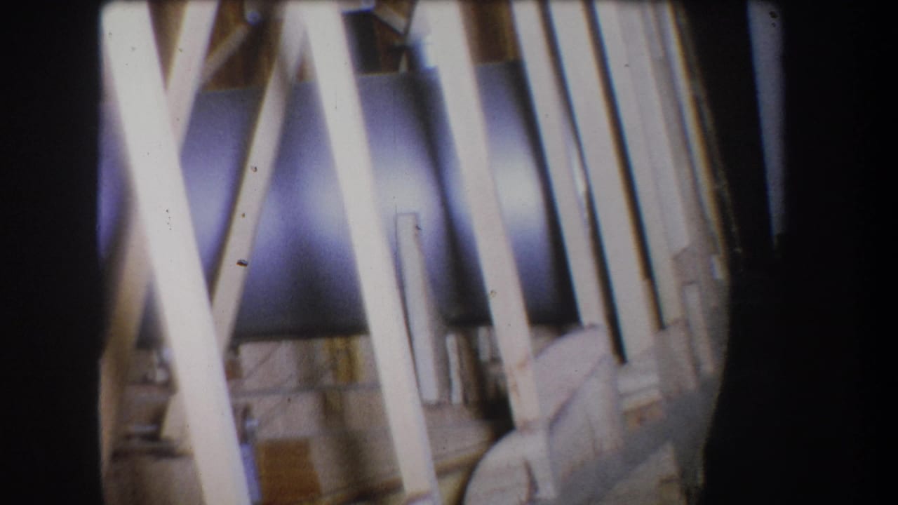 Crossed wooden beams in front of a dark cylindrical metal surface.