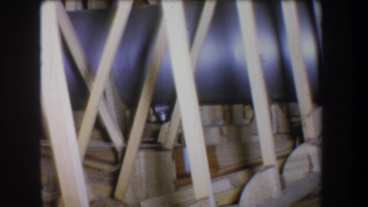 1965 Yucaipa 8mm frame showing crossed pine braces, wood planks, and a silver metal pipe in a shadowed structural interior.