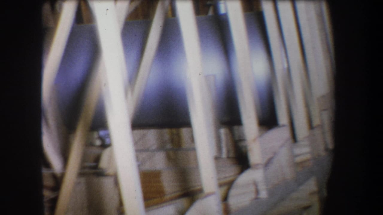 Close 8mm view of pale wood framing, angled braces, and small metal fittings in the Yucaipa construction-detail clip.