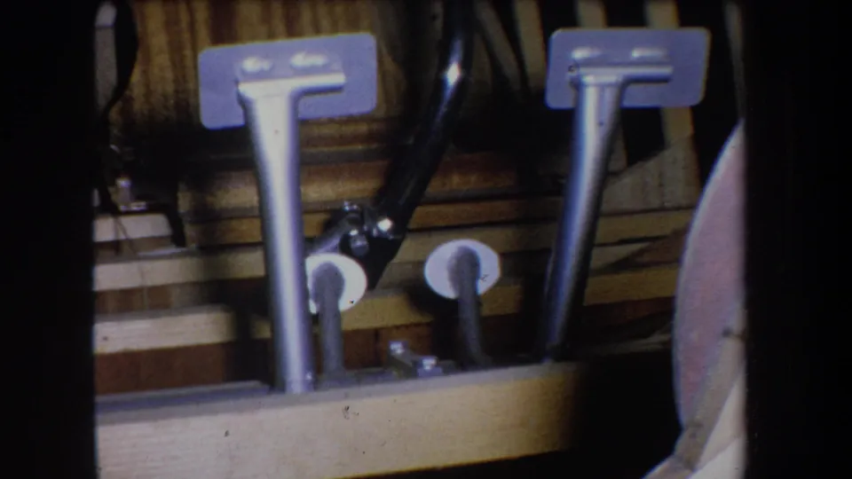 Close 8mm frame showing silver metal pipes, rectangular brackets, black tubing, and wood backing in the Yucaipa structure.