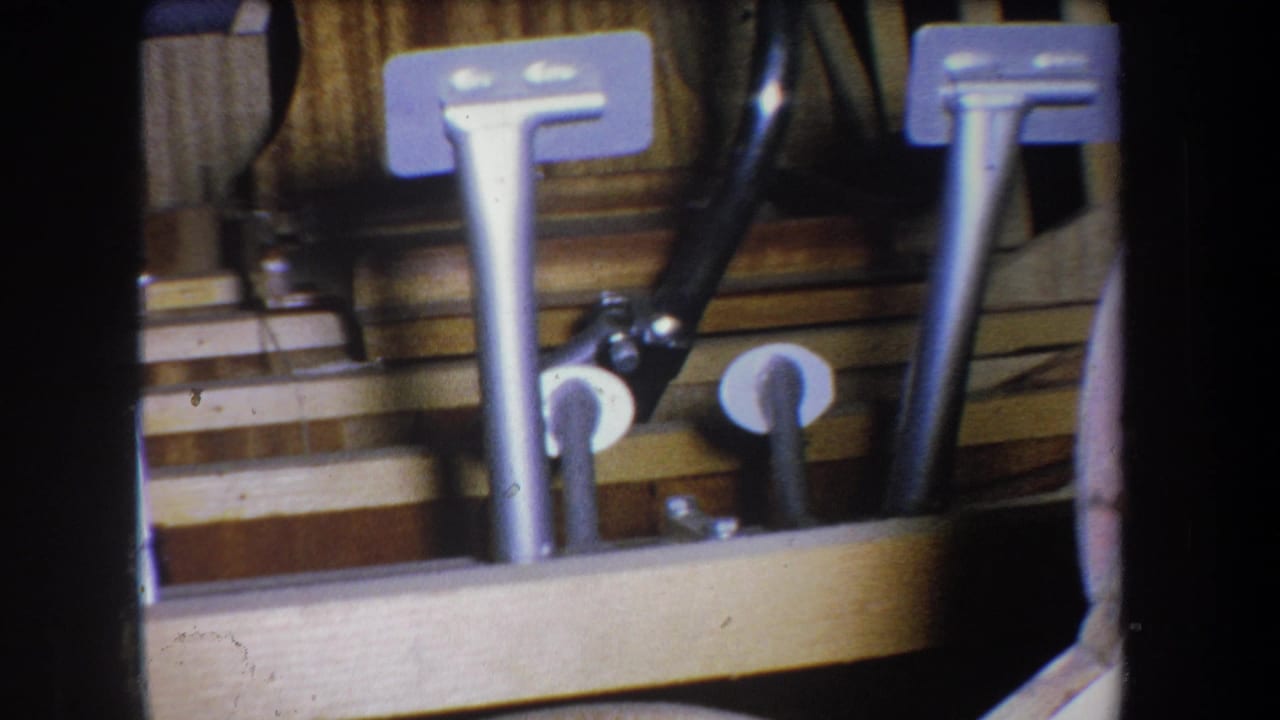 The second frame holds on the paired metal pedals and wooden structure, with warm faded color and 8mm grain.