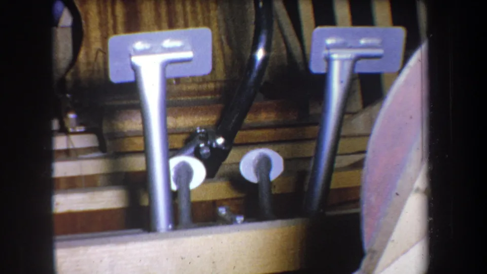 The final frame remains on the pedal mechanism, with two metal pedals, black linkage, layered wood, and a curved side piece visible.