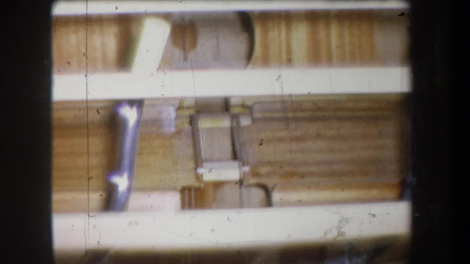 Soft, blurred 1965 Yucaipa 8mm frame with pale horizontal rails, wood paneling, and part of a metal pipe or lever.