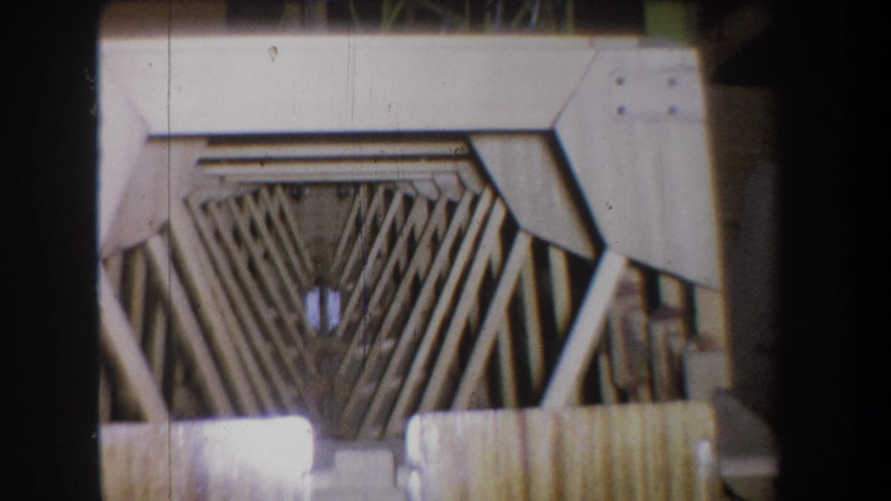 Close view of pale metal framing with V-shaped rods seen through dark film edges.