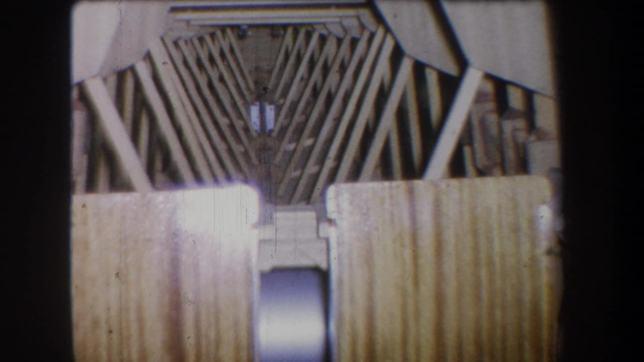 1965 8mm frame from Yucaipa-area footage showing wooden ribs, angled braces, and pale planking inside a vessel-like structure.