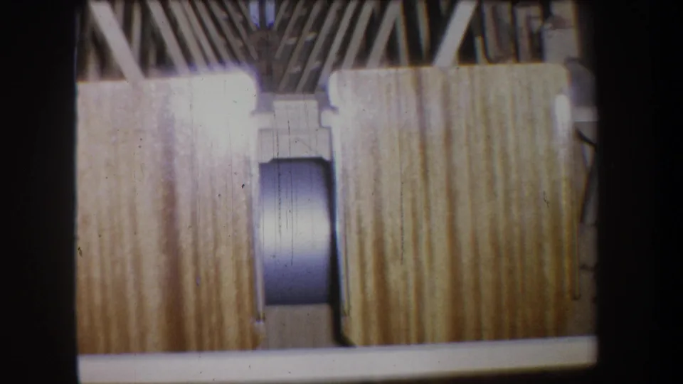 1965 home-movie frame showing planked wood surfaces, ribbed framing, and a rounded cylinder within the boat-like construction.