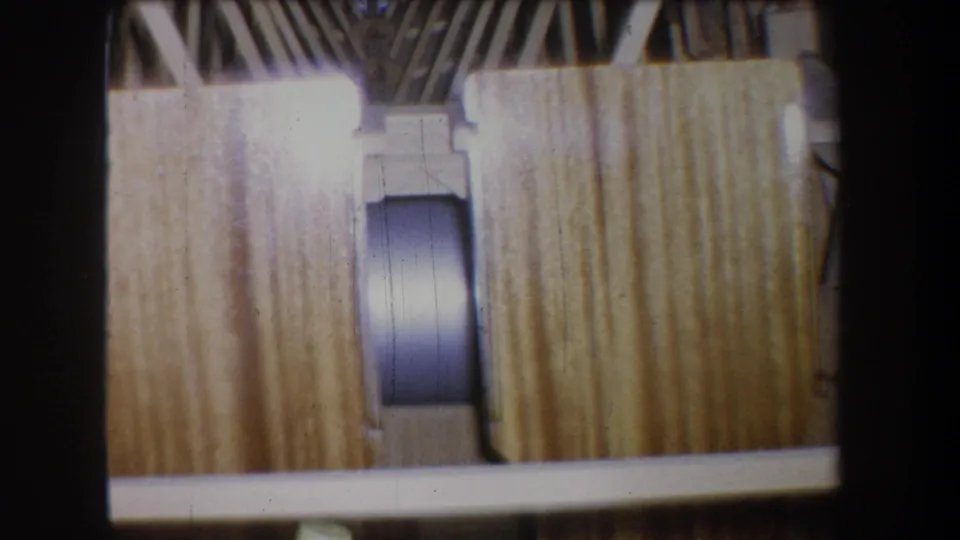 1965 8mm still showing a close interior view of wooden planking, braces, and a rounded component in a vessel-like frame.