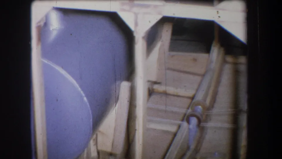 1965 8mm frame from Yucaipa showing a large painted tank beside angled piping and simple industrial support structures.